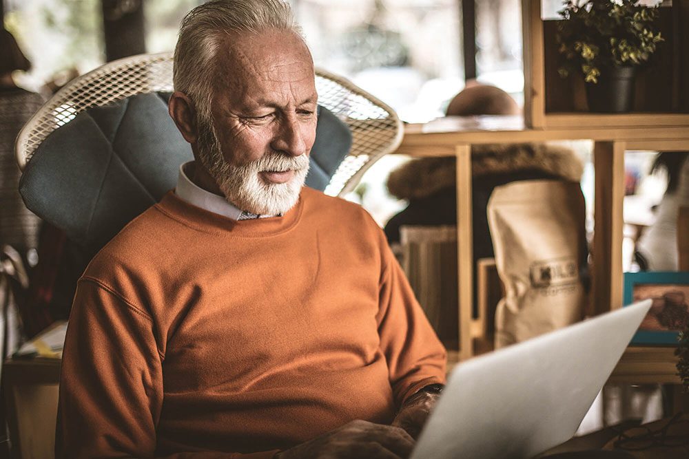Senior man in orange sweater on computer